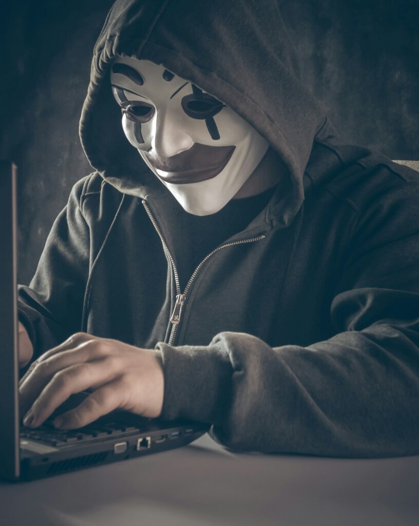 Anonymous computer hacker in white mask and hoodie. Using laptop computer for cyber attack and calling on cellphone. Special photo processing film grain, noise. More of my photos and videos Adobe Stock:http://bit.ly/3RqlciK More of my photos and videos Shutterstock: https://www.shutterstock.com/g/ALEKSANDRBERDYUGIN My email: bermix999@gmail.com