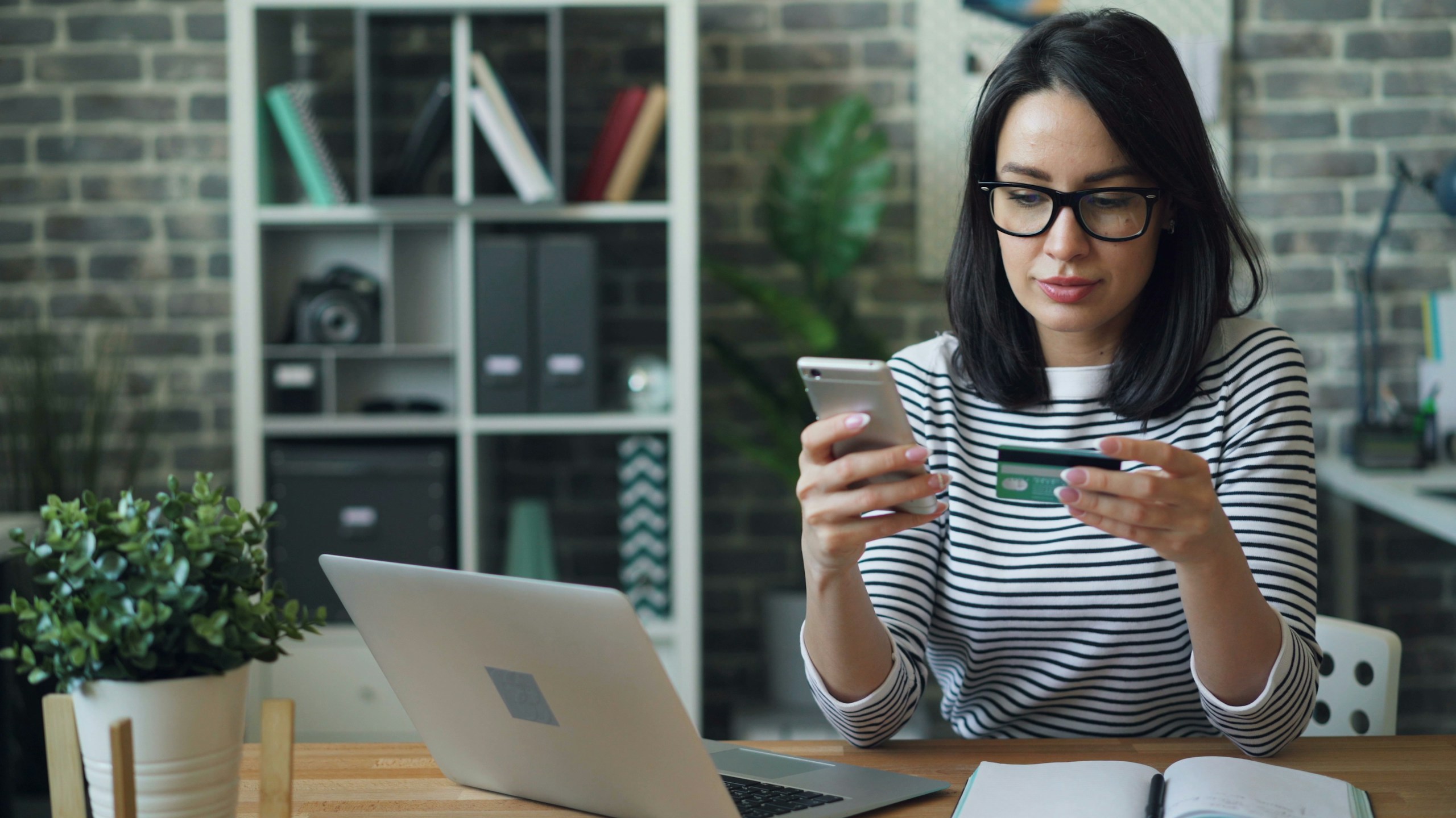 Portrait of young woman making payment with credit card using smartphone at work