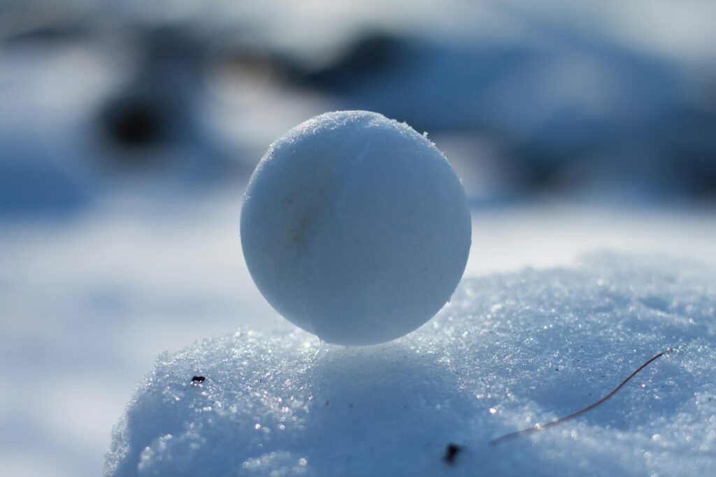 A packed snow ball sits on top of a snow drift.