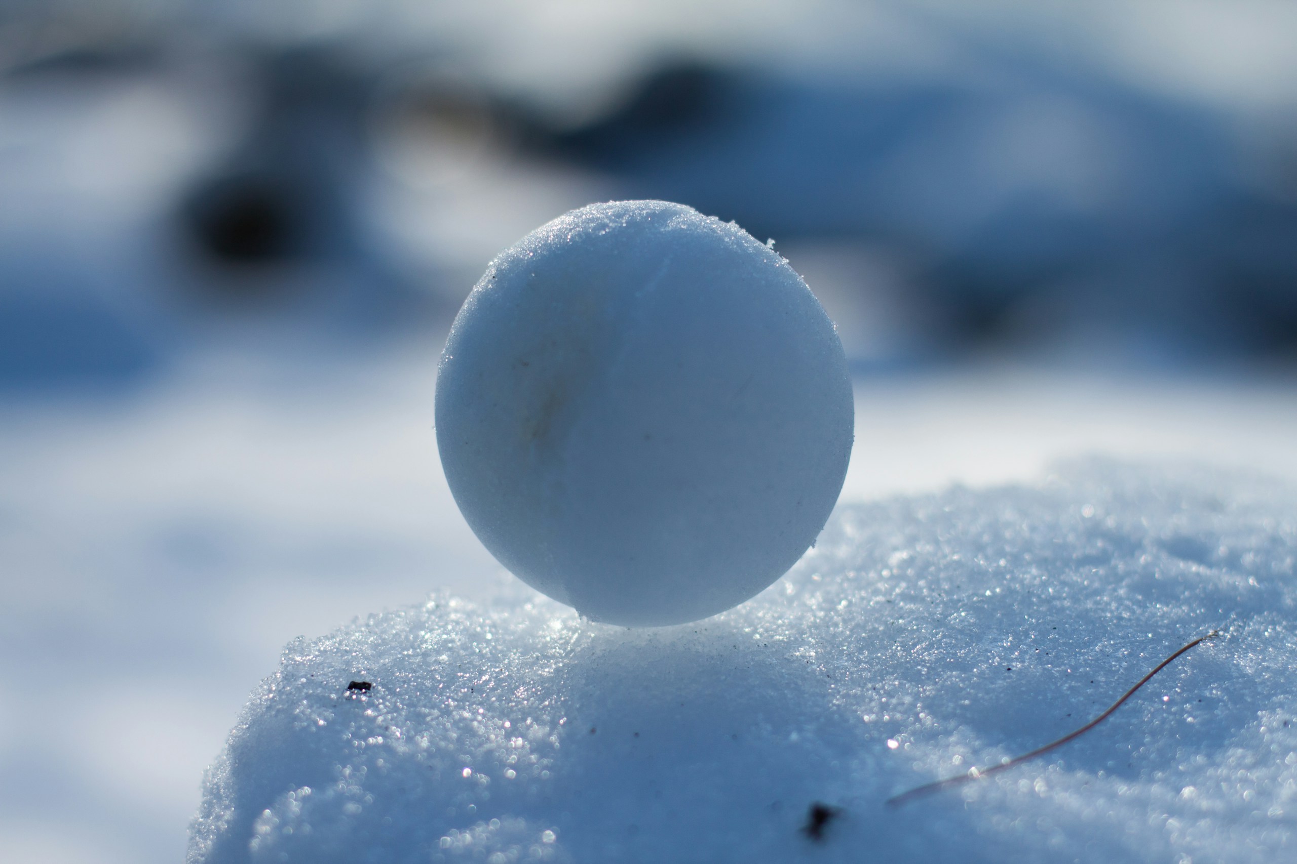 A packed snow ball sits on top of a snow drift.
