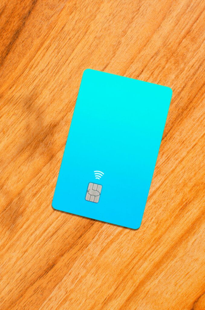 Blue credit card with a visible chip on top of a wooden table with soft lights and shadows. Concept: finance, purchases, payments, loans, spending, investments and debts.