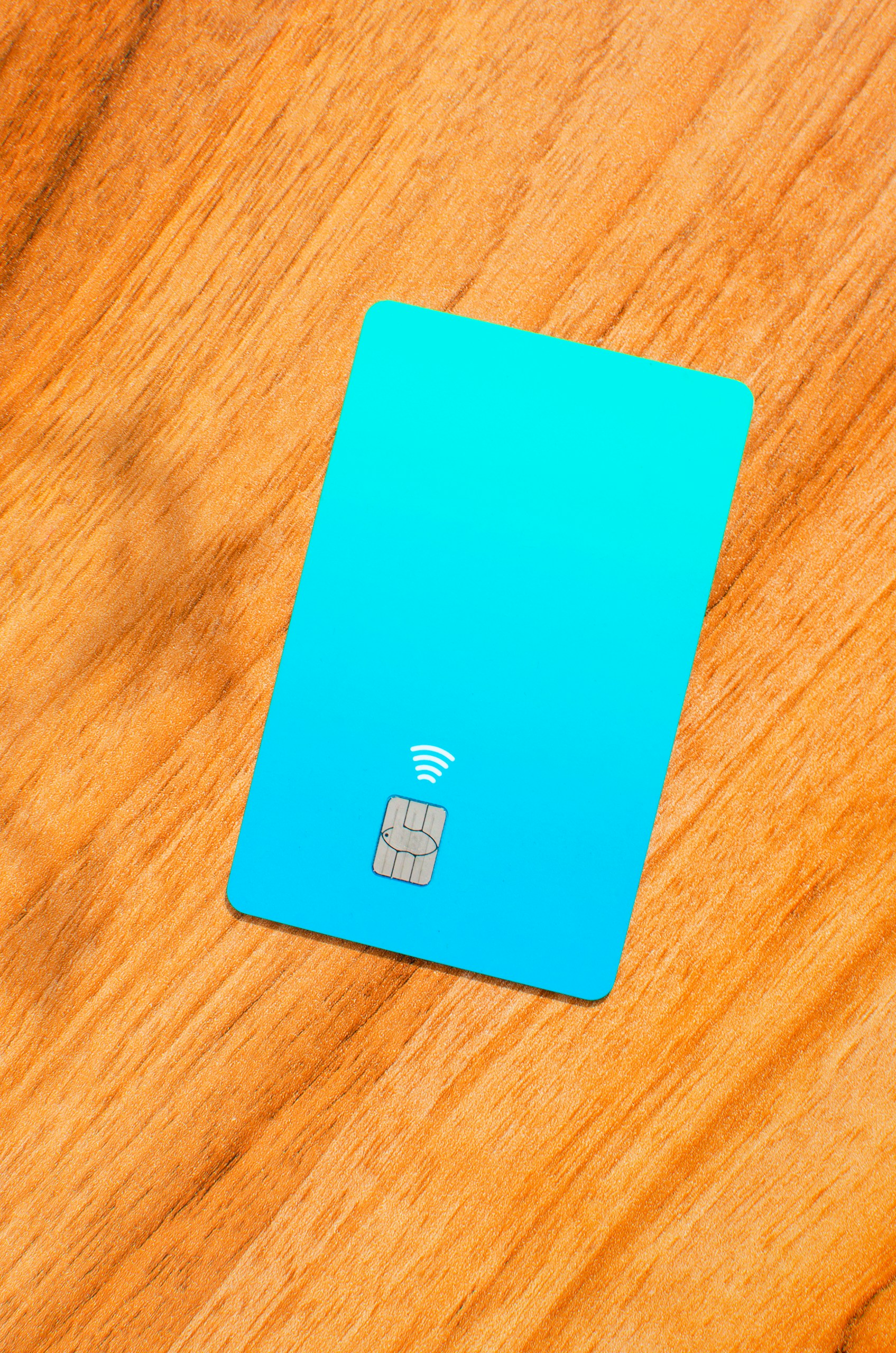 Blue credit card with a visible chip on top of a wooden table with soft lights and shadows. Concept: finance, purchases, payments, loans, spending, investments and debts.