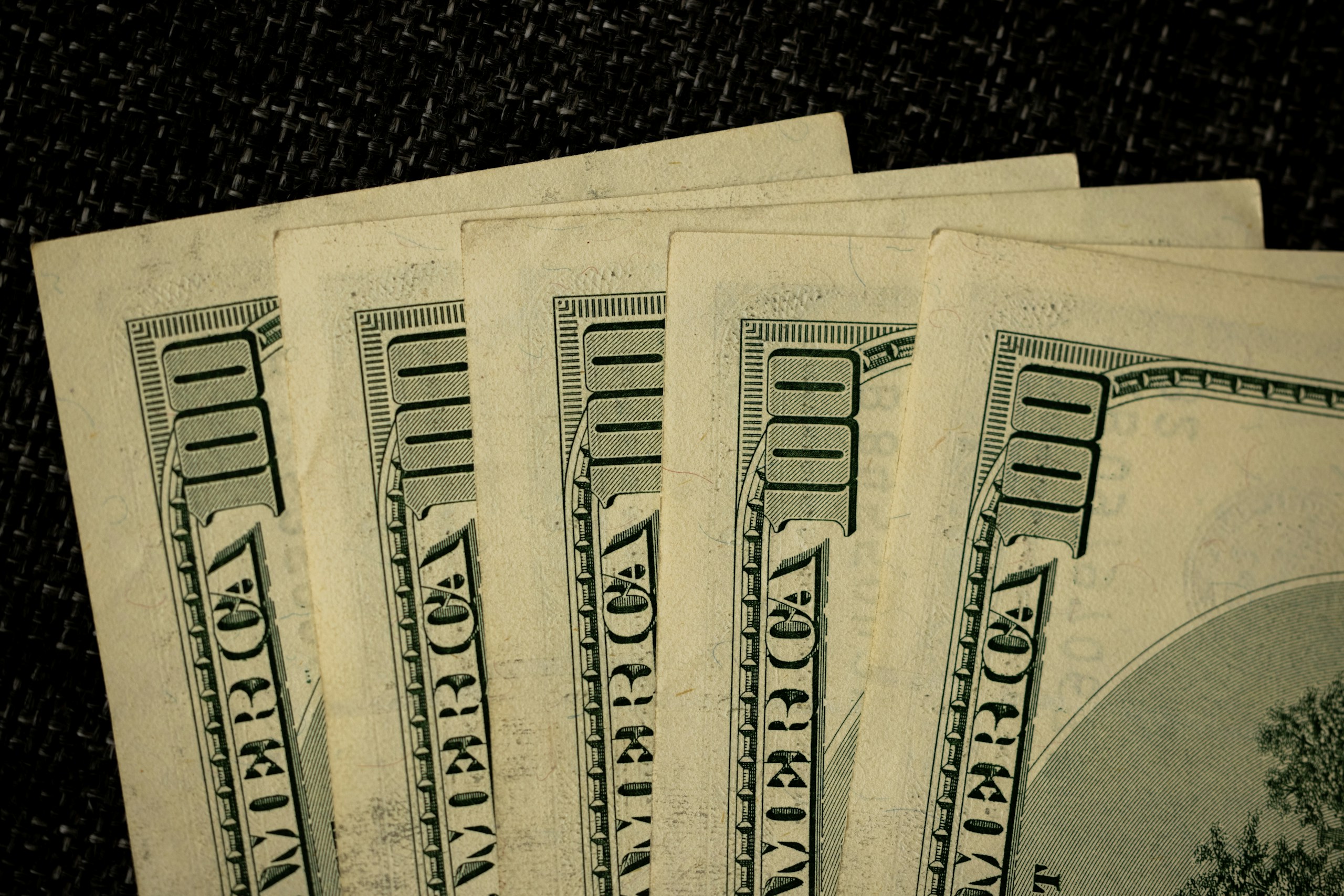 Fanned stack of US $100 bills on a dark textured background