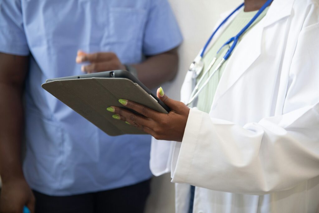 Two healthcare professionals—one in a white coat with a stethoscope and the other in blue scrubs—reviewing content on a tablet device.