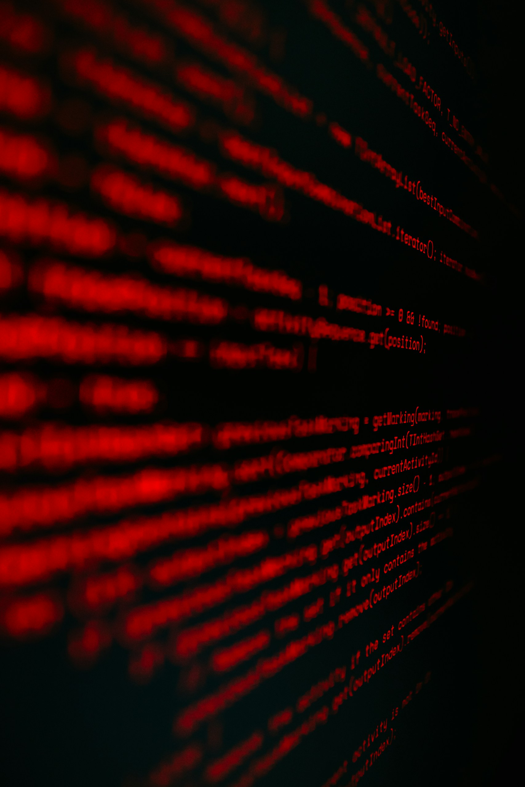 Red programming code on a dark background, close-up perspective of scrolling lines.
