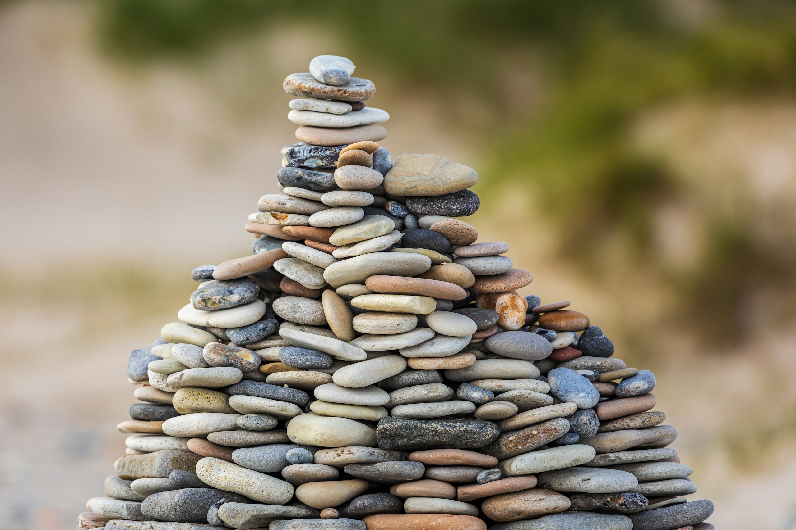 Stack of smooth pebbles balanced into a cairn outdoors, with a blurred natural background.