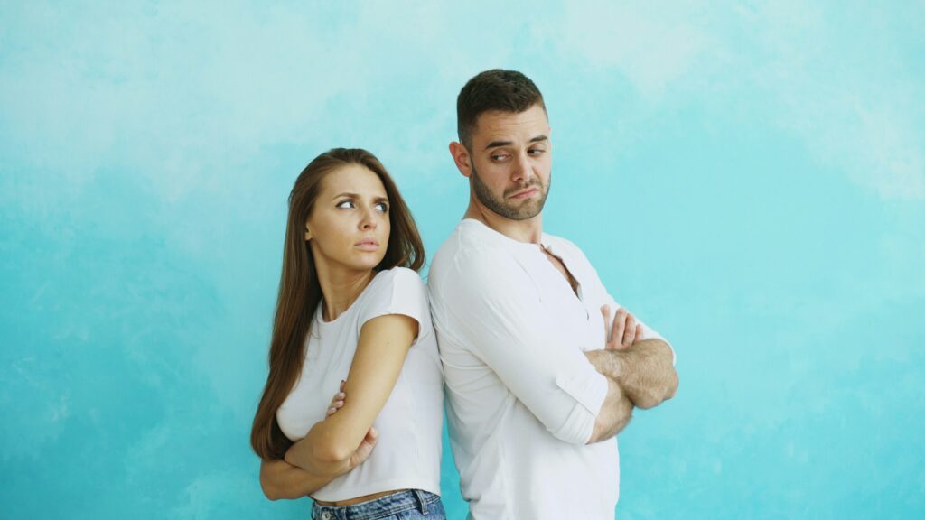 Young couple upset and angry each other standing back to back on blue background