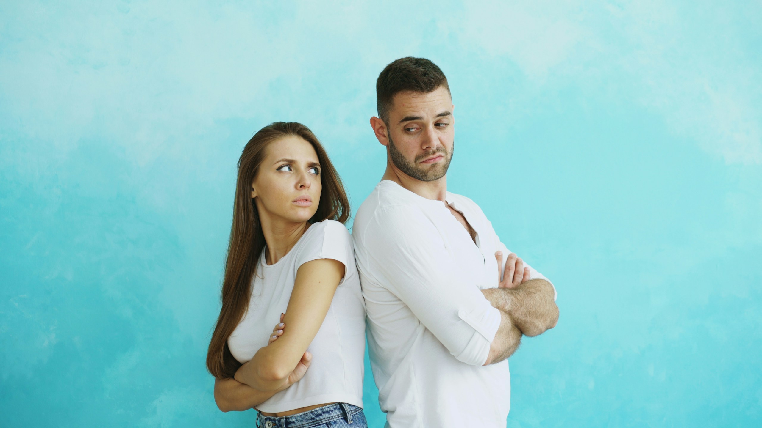 Young couple upset and angry each other standing back to back on blue background