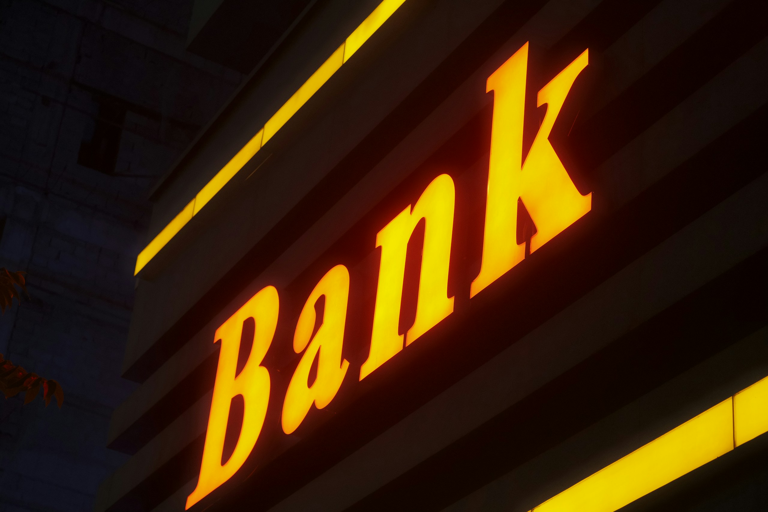 Close-up of a glowing orange neon sign with cursive letters against a dark storefront backdrop at night.