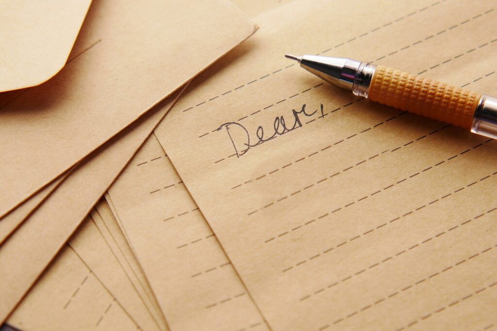 Close-up of a fountain pen nib resting on tan lined paper with the handwritten word 'Dear' in cursive.