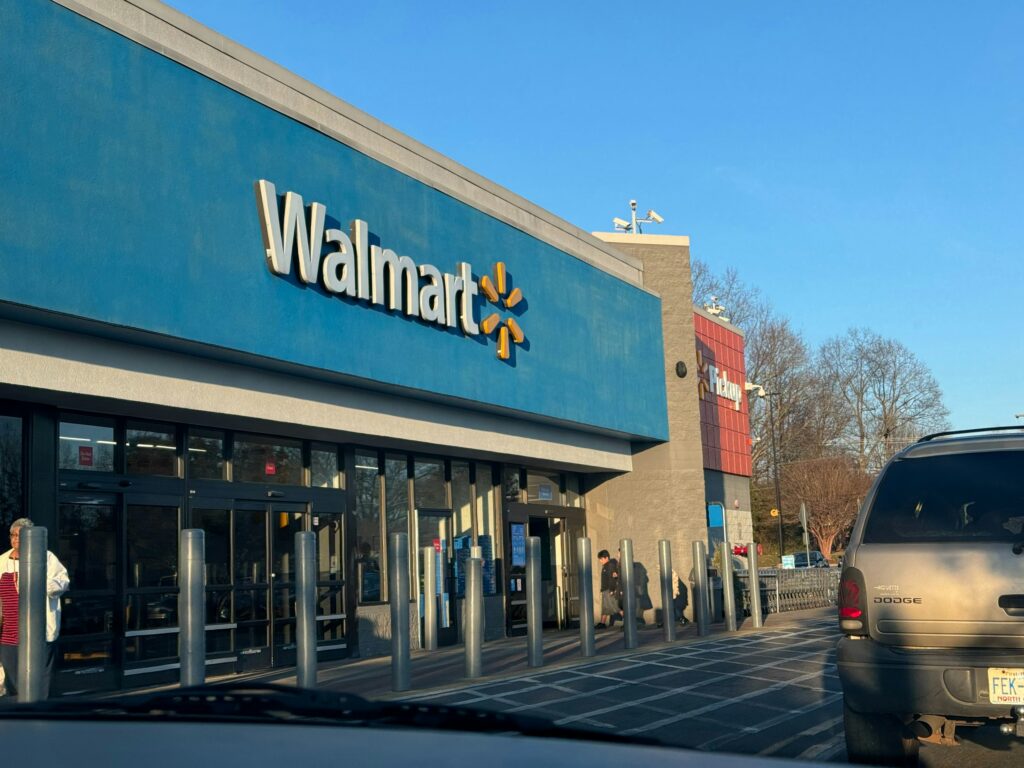 Front view of a Walmart store with a blue façade and large white Walmart lettering; a grey SUV is parked at the curb in the foreground.