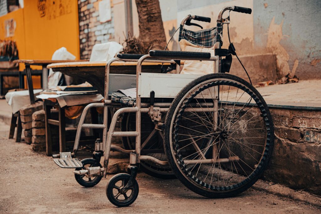 Wheelchair attached to a flatbed cart in a gritty alley with peeling walls and orange tones in the background.