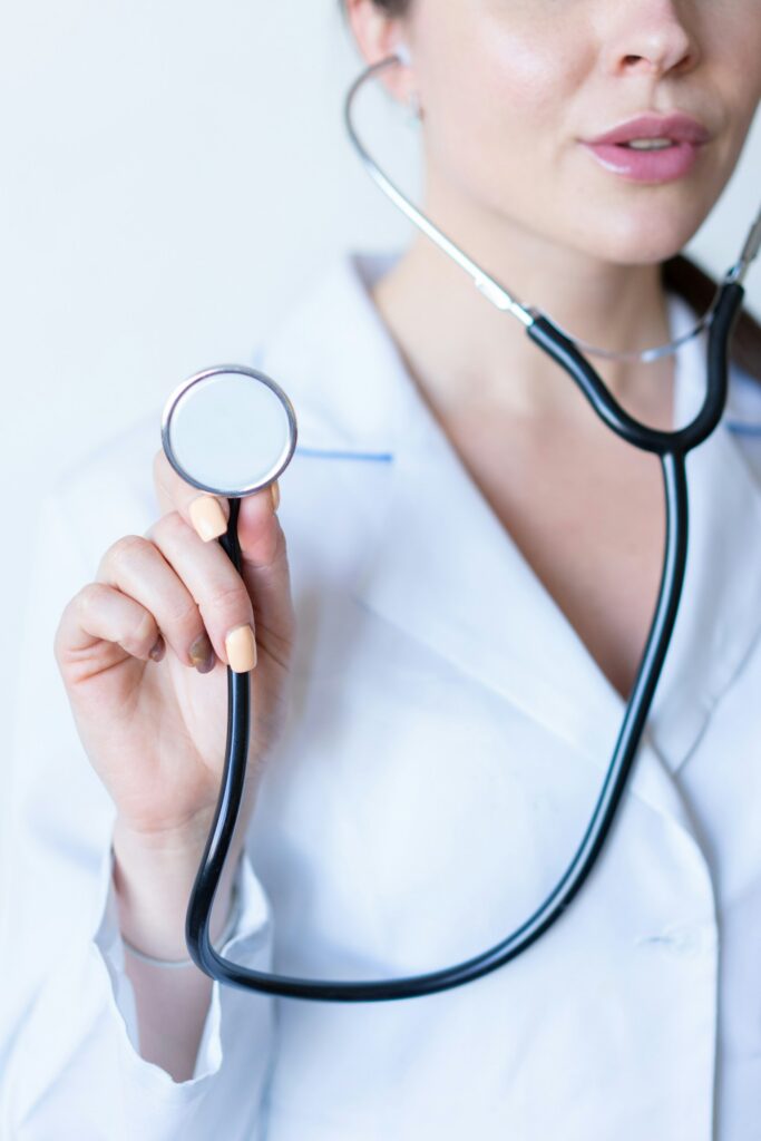 Medical professional holding a stethoscope toward the camera with a white lab coat visible at the edges.