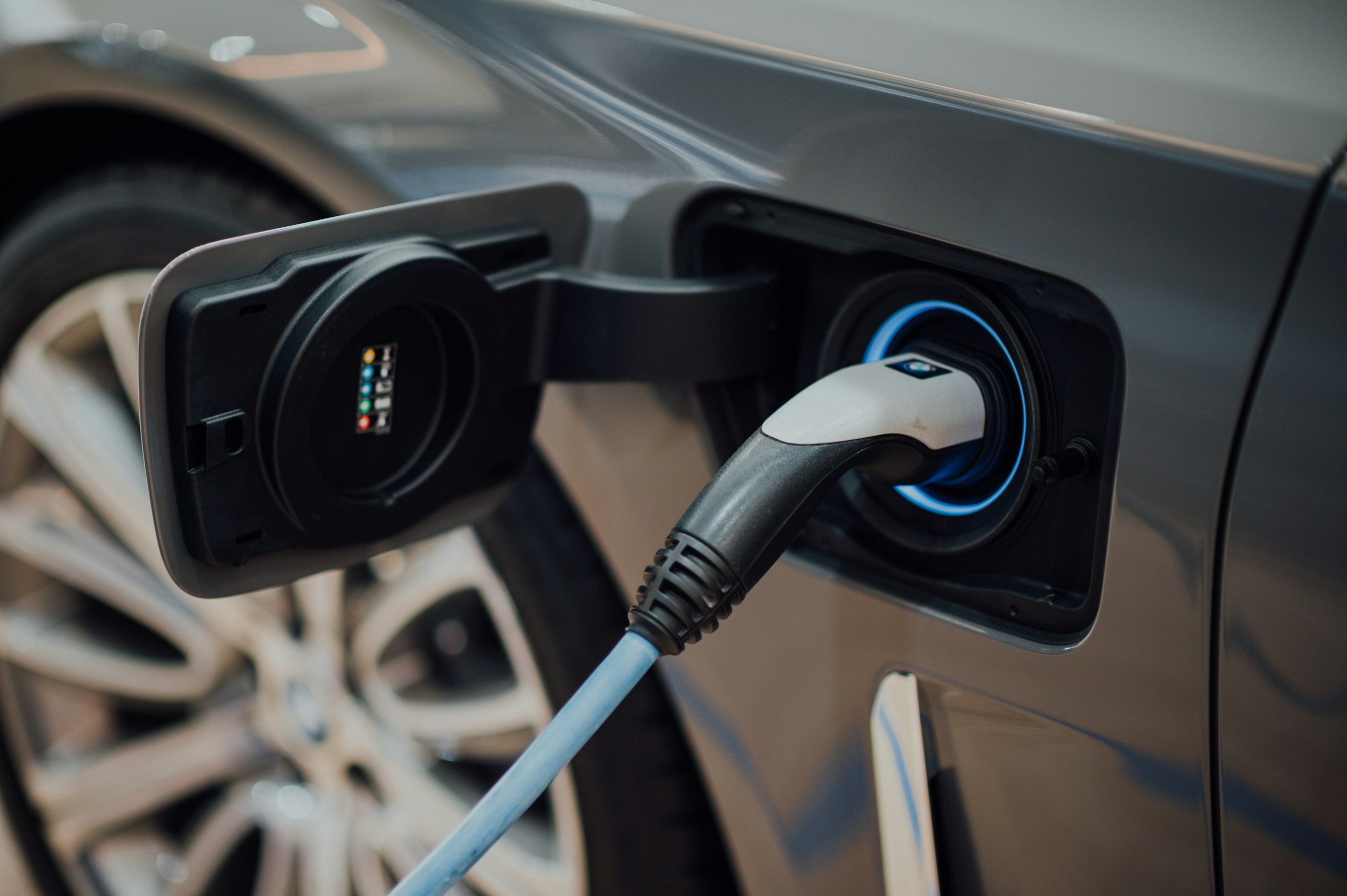 Car charging port with a blue-lit ring; a charging cable is connected to the vehicle.
