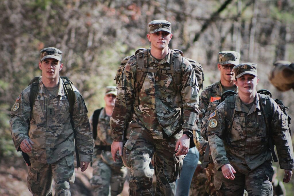 Group of soldiers in camouflage uniforms walking through a wooded area.
