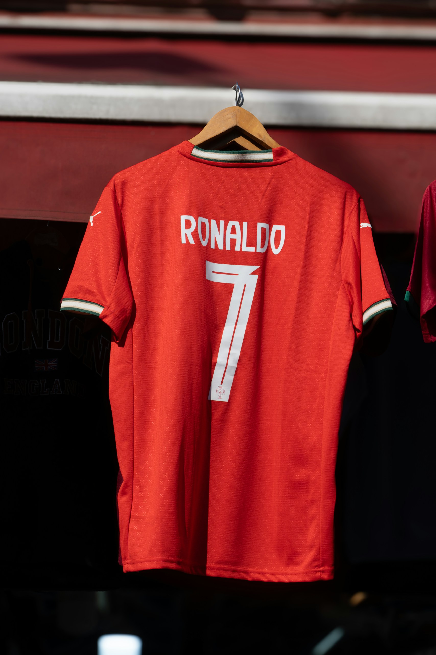 Red Ronaldo football jersey with number 7 hanging on a wooden hanger against a dark background.