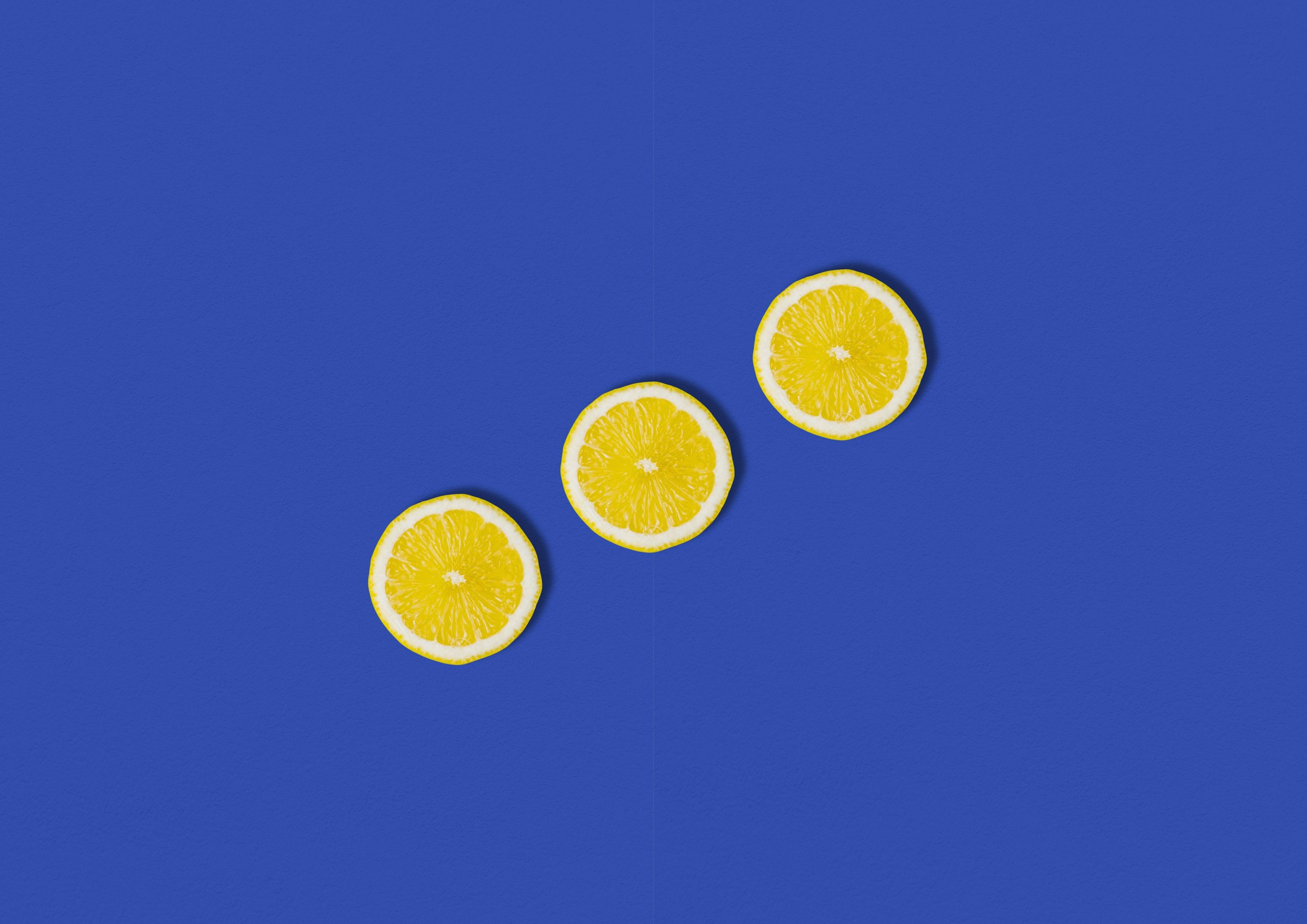 Five yellow lemon slices arranged diagonally on a vivid blue background for decorative contrast, forming a curved line across the bottom-right.
