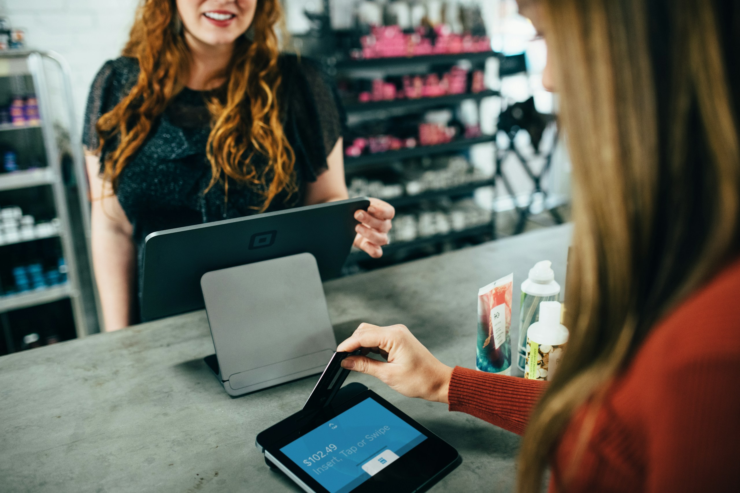 Customer pays at checkout using a contactless card reader while the cashier assists nearby.