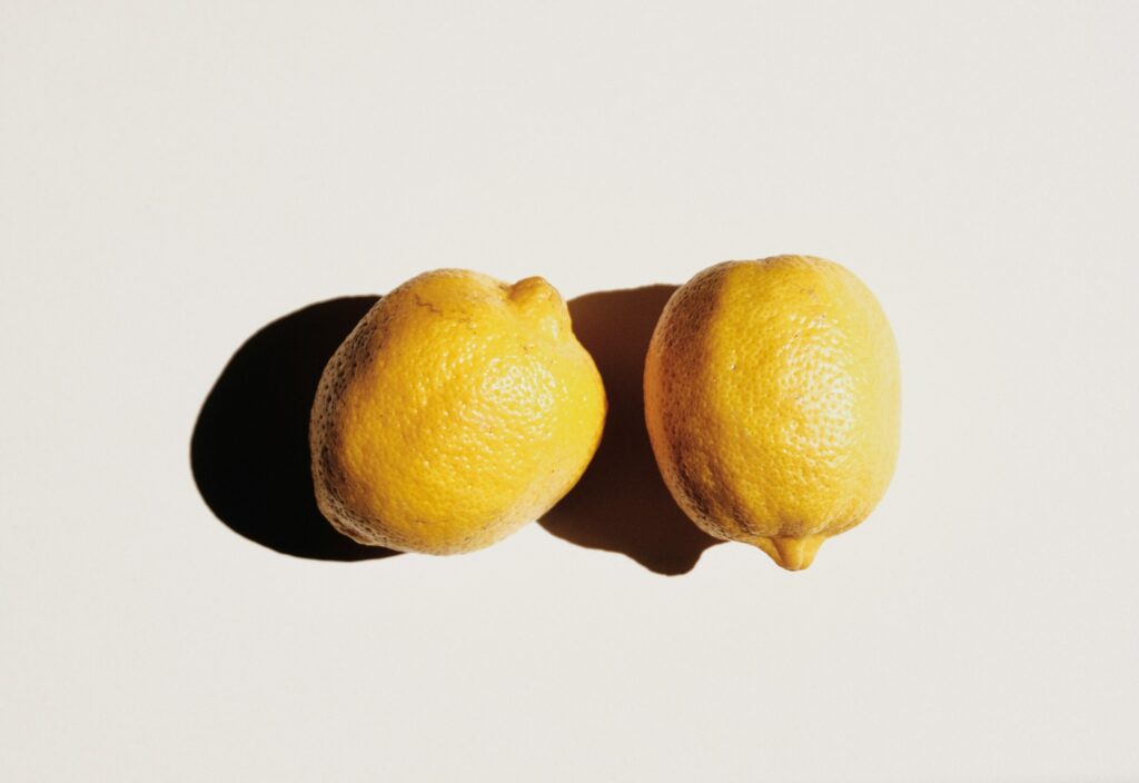 Two bright yellow lemons resting together on a pale background with a soft shadow nearby