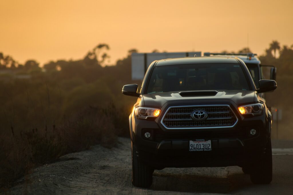 Front view of a Toyota pickup on a dirt road at sunset, with a warm orange sky and blurred trees in the background.