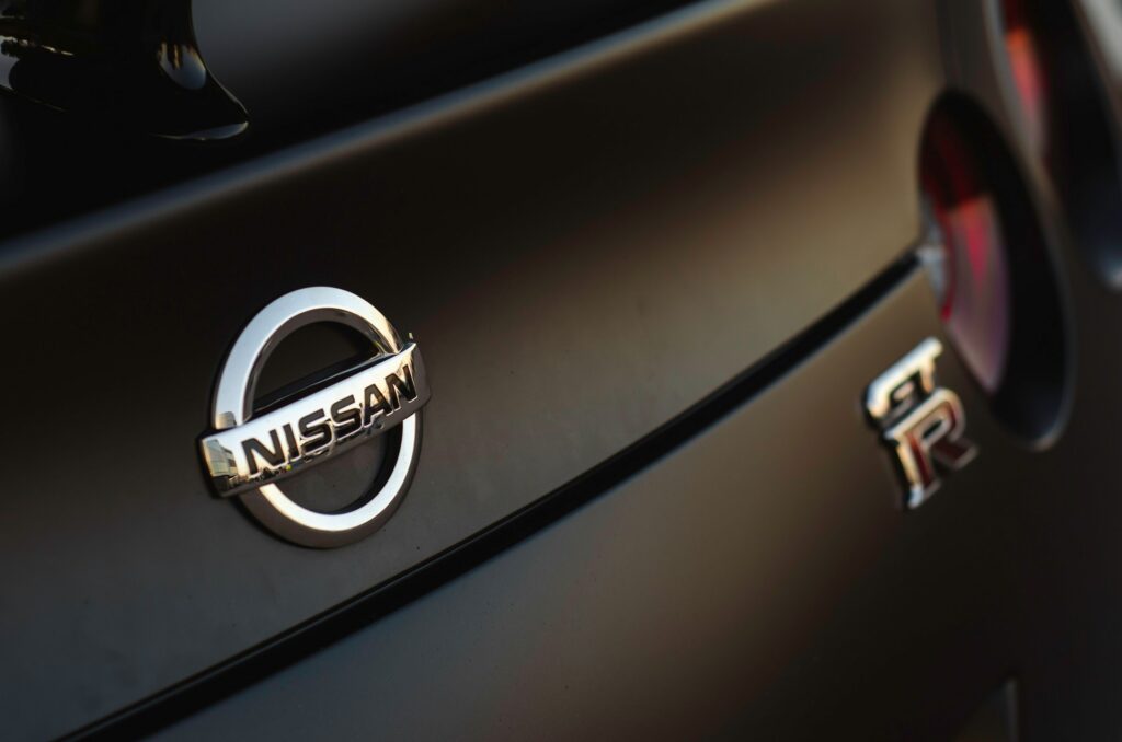 Close-up of the Nissan emblem on the rear of a dark car, with a blurred taillight in the background.