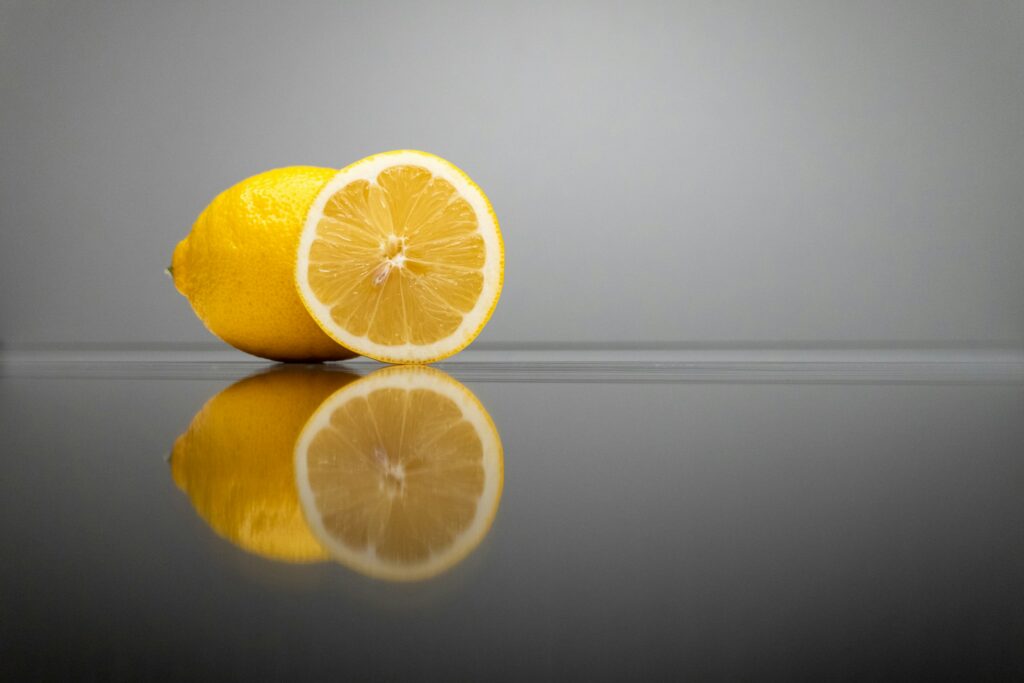 Yellow lemon cut in half resting on a reflective surface with a gray background