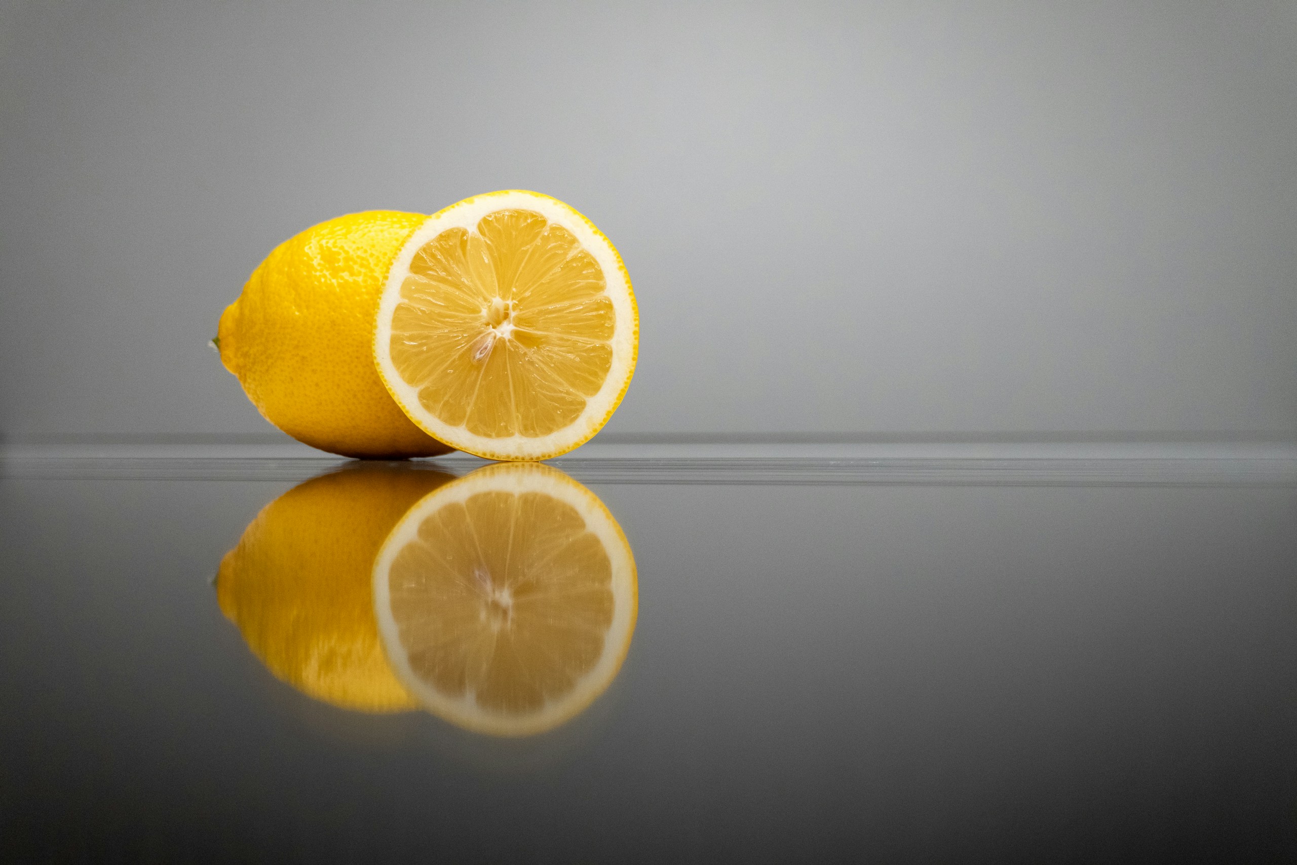 Yellow lemon cut in half resting on a reflective surface with a gray background