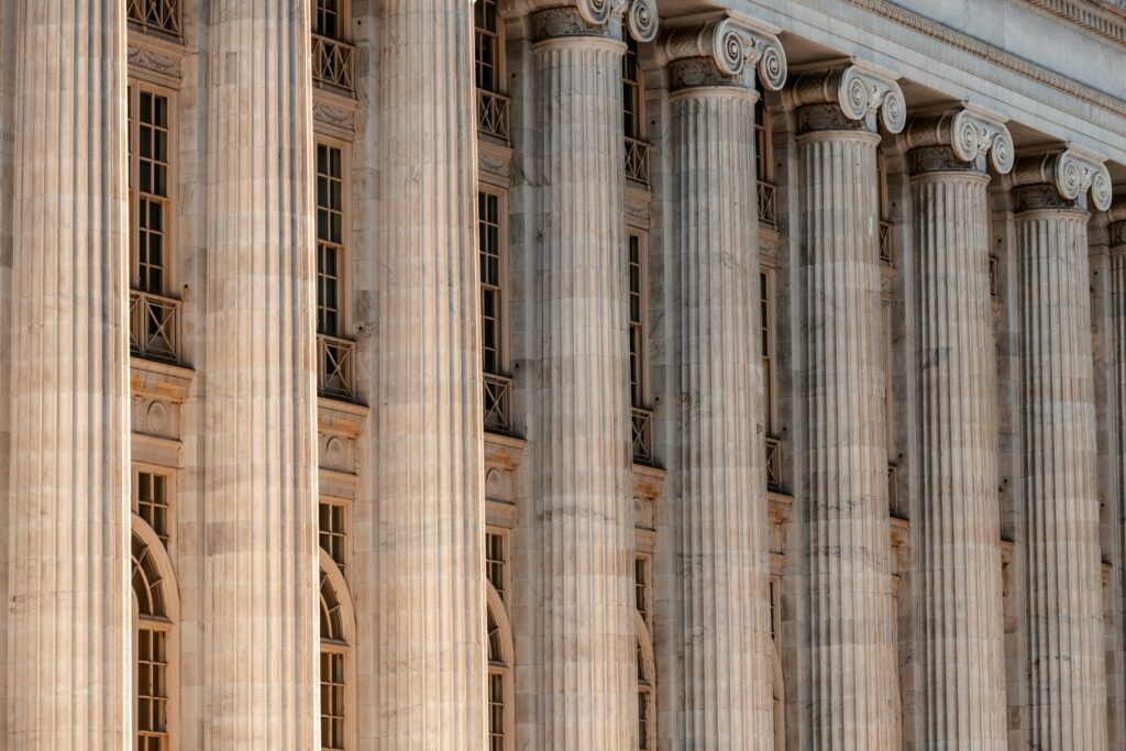 Row of tall fluted marble columns with Ionic capitals on a classical building façade, with narrow windows between them.