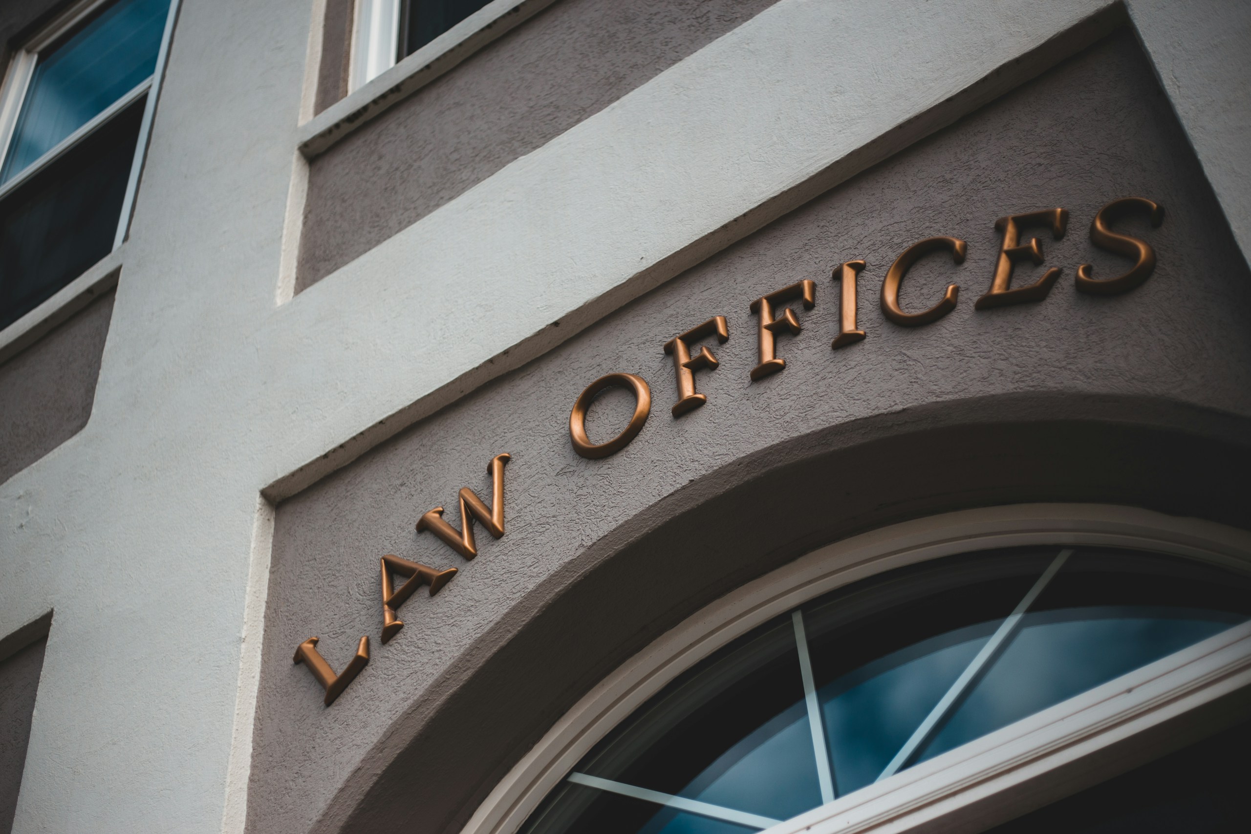 Bronze letters spelling 'OFFICES' mounted on a light brown wall above a curved window/entryway.