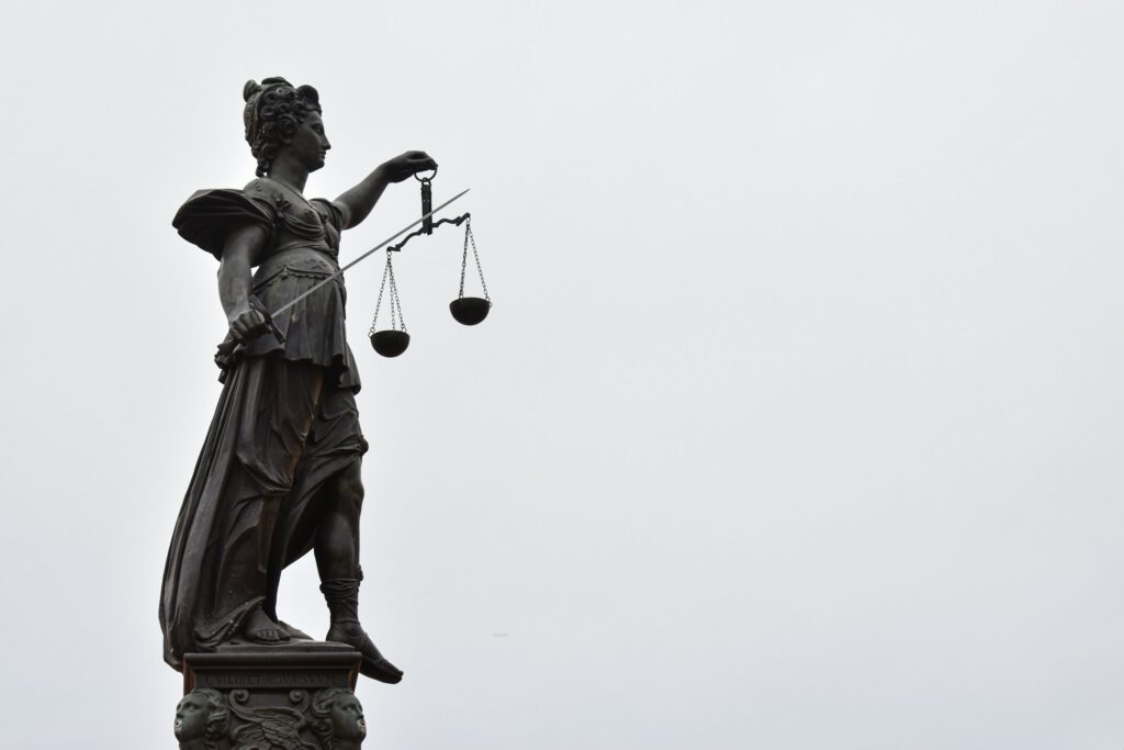 Bronze statue of Lady Justice holding a balance scale against a gray sky.
