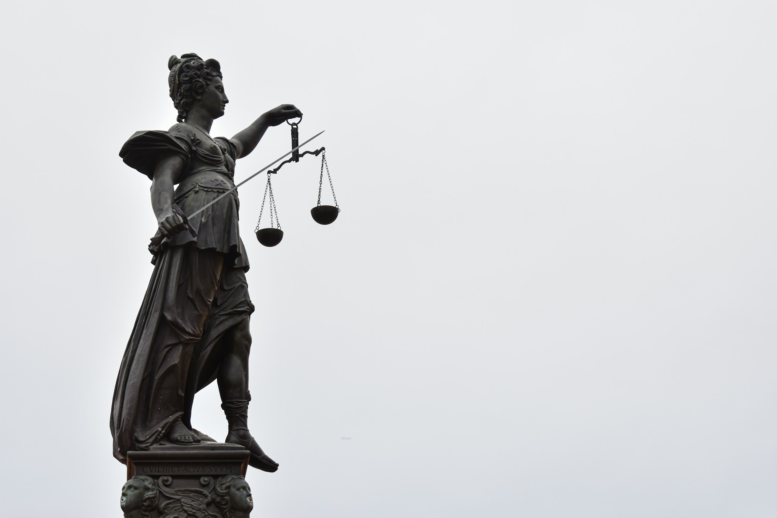 Bronze statue of Lady Justice holding a balance scale against a gray sky.