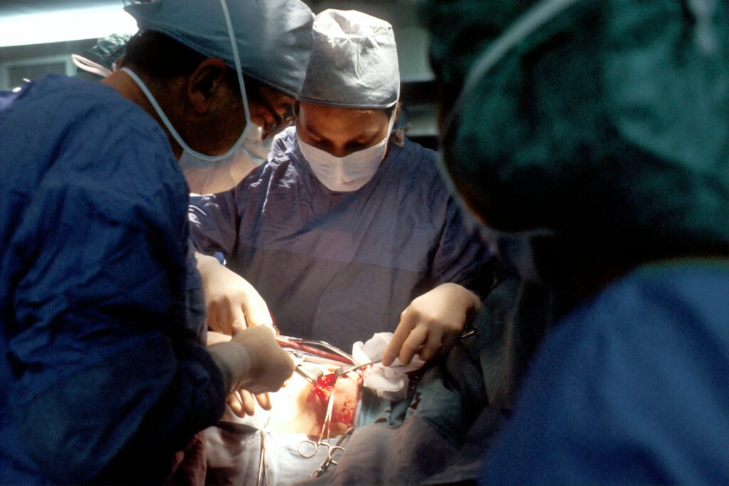 Biopsy. A Caucasian woman patient is being operated on. Her nipple is being incised by the surgeon. The male surgeon and an operating room attendant are visible. A surgical biopsy is being performed to determine exact nature of solid tumor. Creator: Linda Bartlett