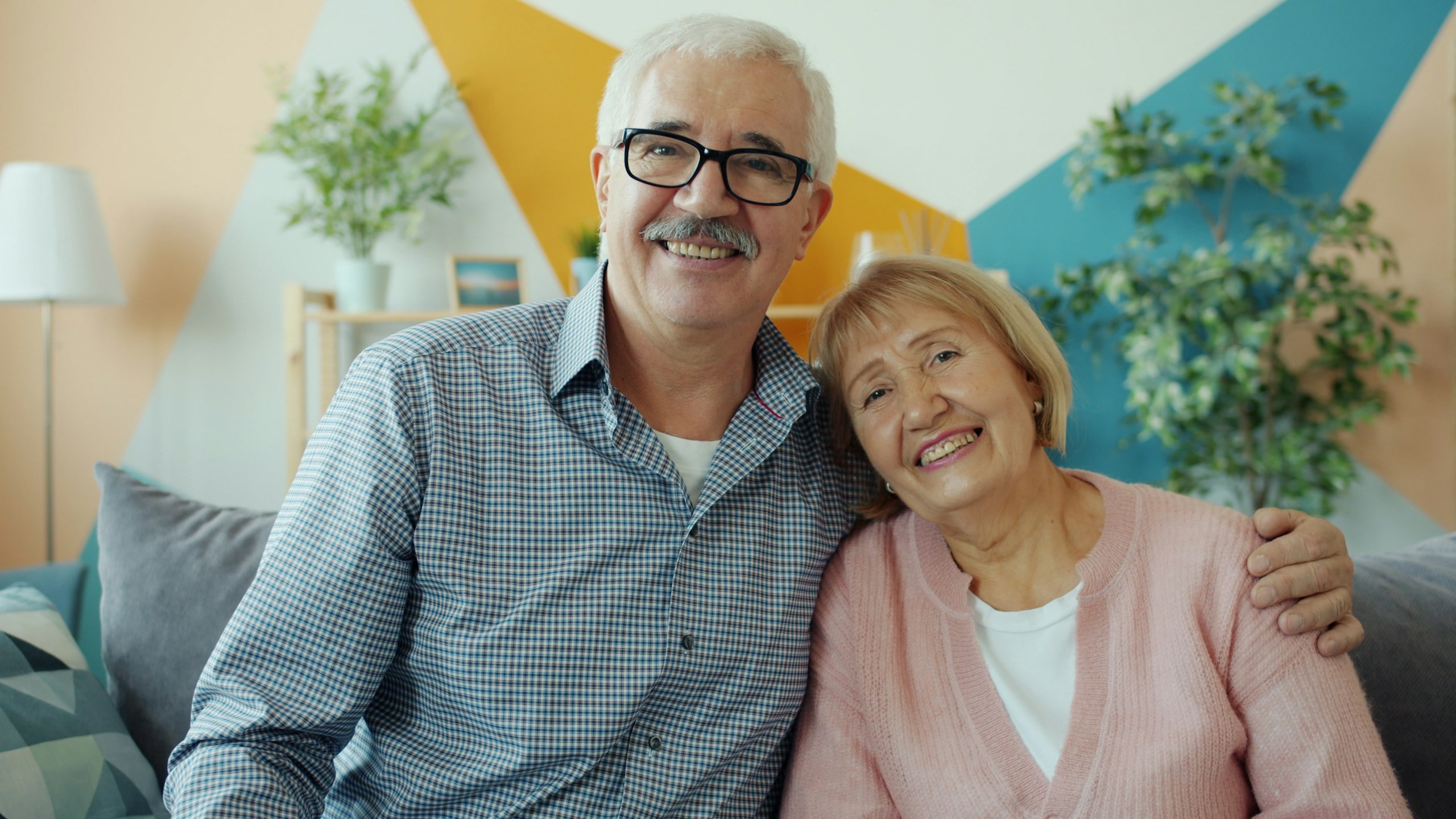 cheerful couple retired man and woman smiling embracing sitting on couch at home. Family life, retirement and happiness concept.