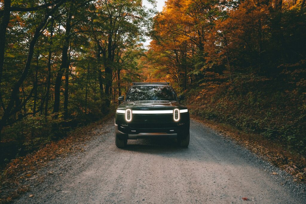 Forest Green Rivian R1T electric truck driving on a gravel road in the blue ridge mountains during fall