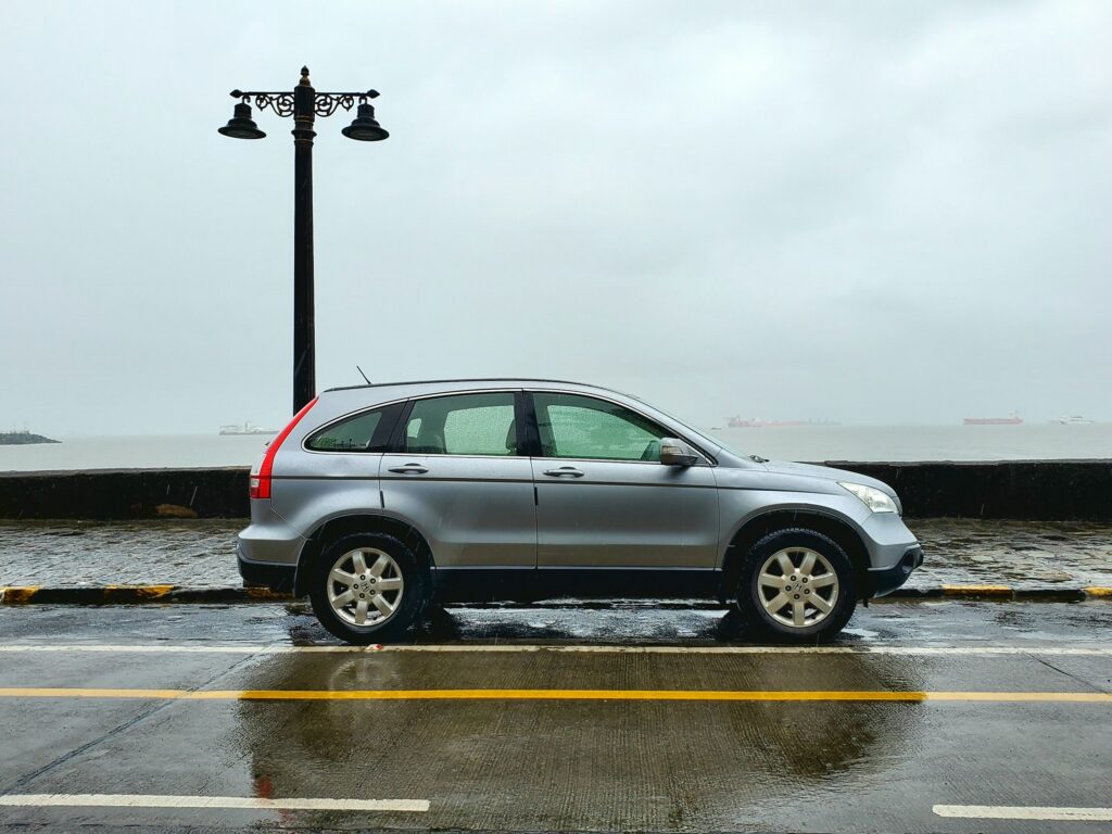 Silver SUV parked along a rainy waterfront with a tall ornate streetlamp behind it.