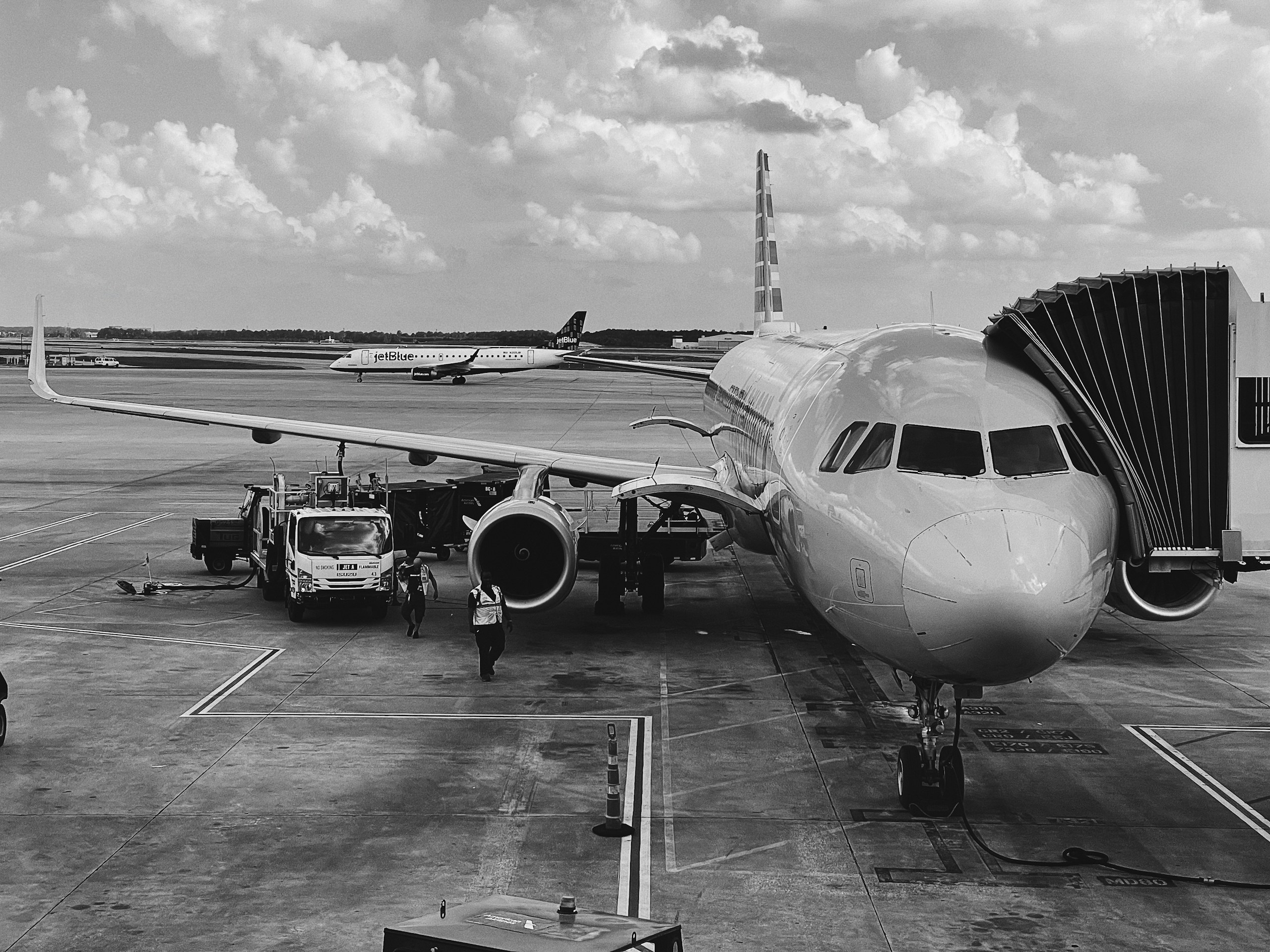 Front view of a JetBlue aircraft docked at a gate with a jet bridge and ground crew on the tarmac.