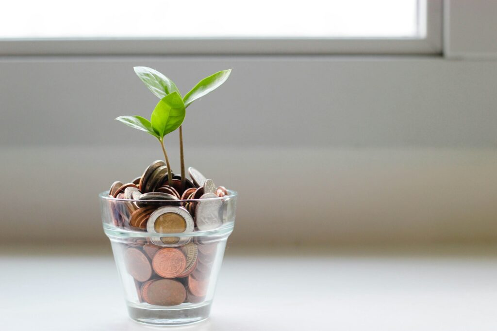 Clear glass filled with coins and a small green sprout growing from the top, symbolizing financial growth.