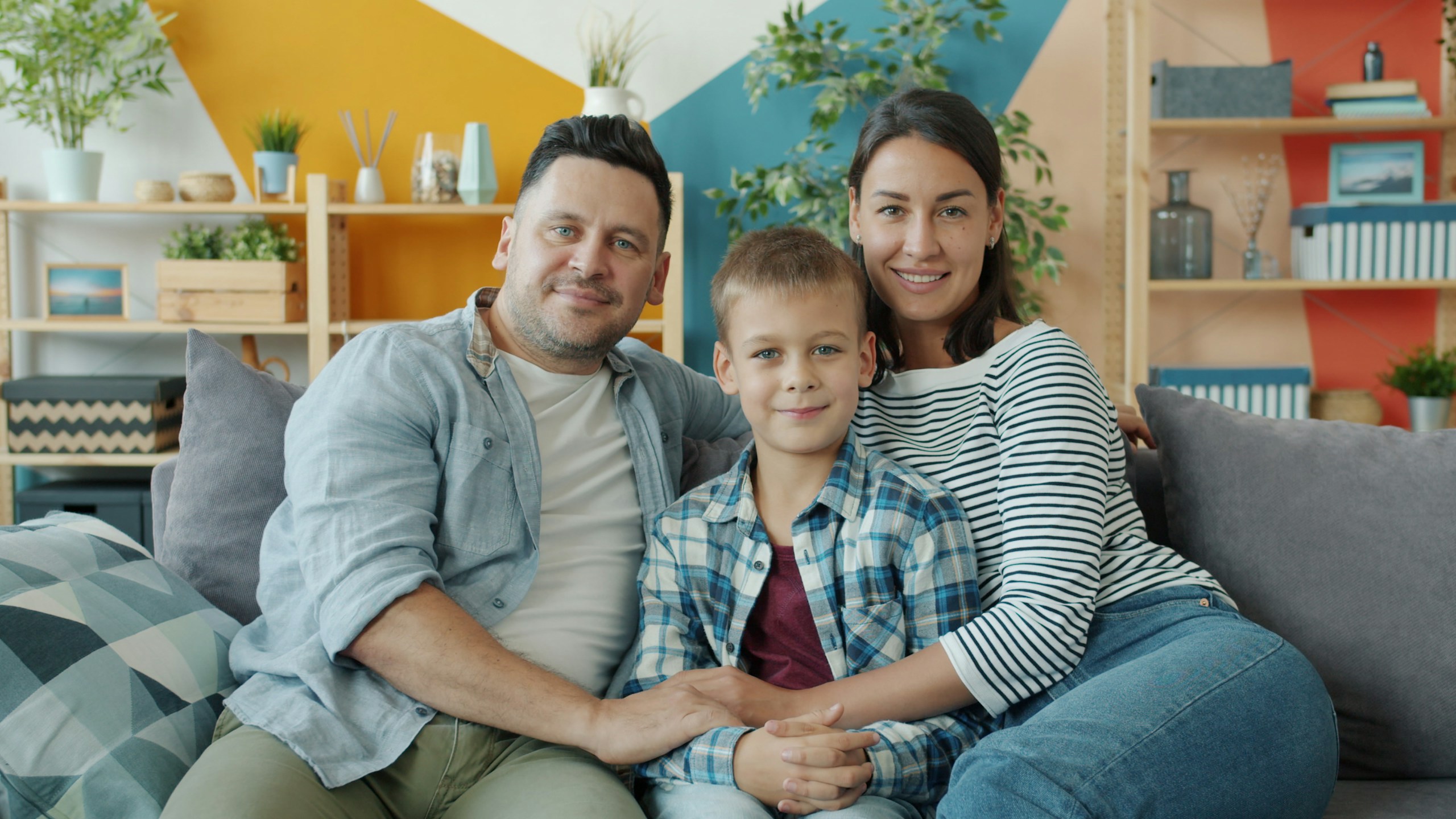 Portrait of happy young family mother, father and son sitting on sofa at home smiling looking at camera. People, lifestyle and togetherness concept.