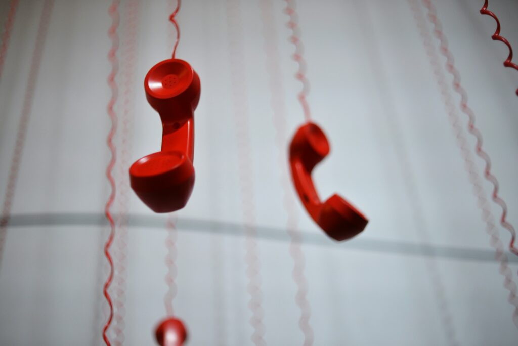 Red telephone handsets are suspended from curling ribbons as festive decor in a soft-lit background.