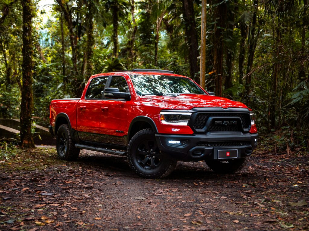 Red RAM pickup truck parked on a leaf-covered path in a dense forest.