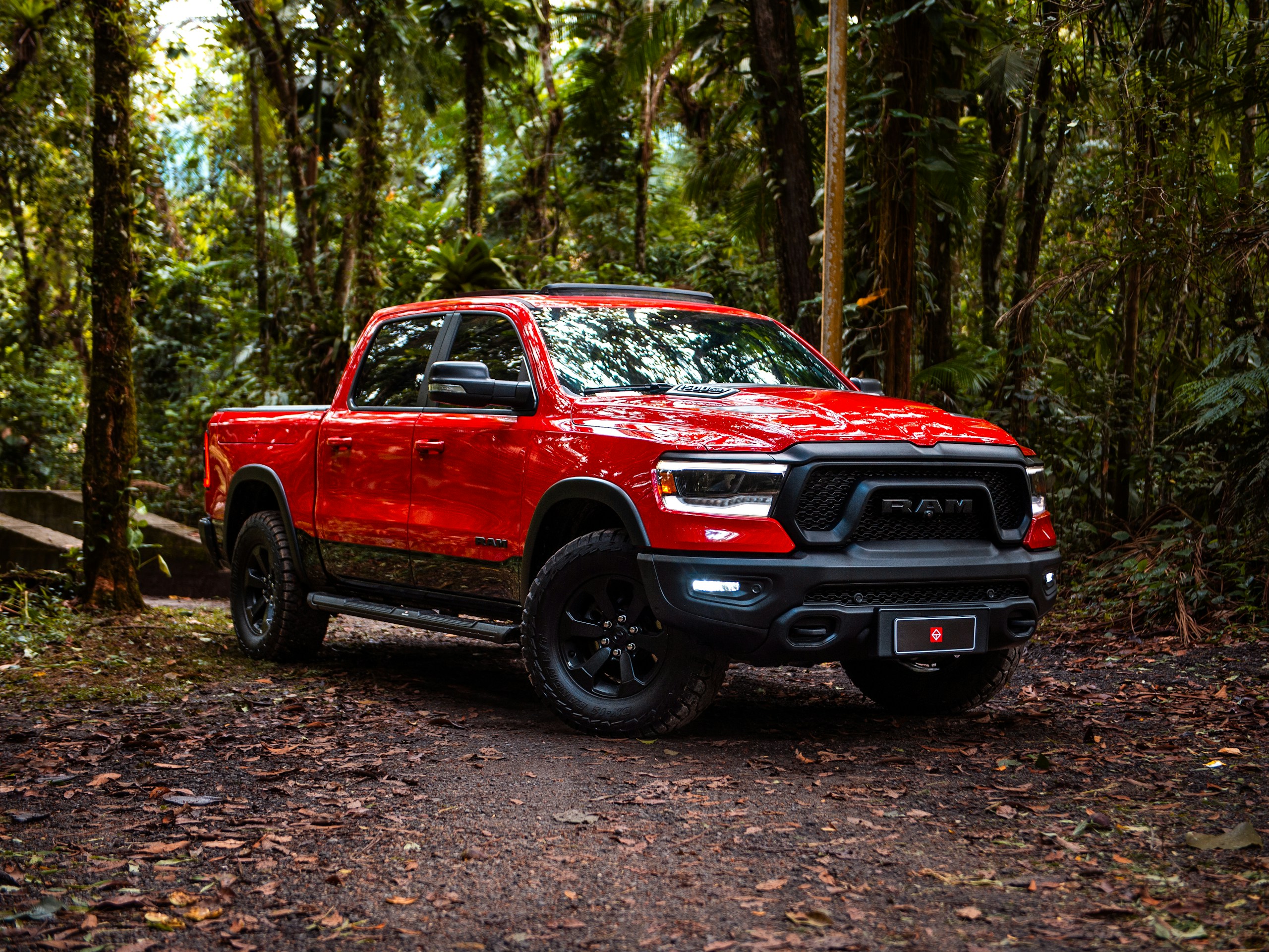 Red RAM pickup truck parked on a leaf-covered path in a dense forest.