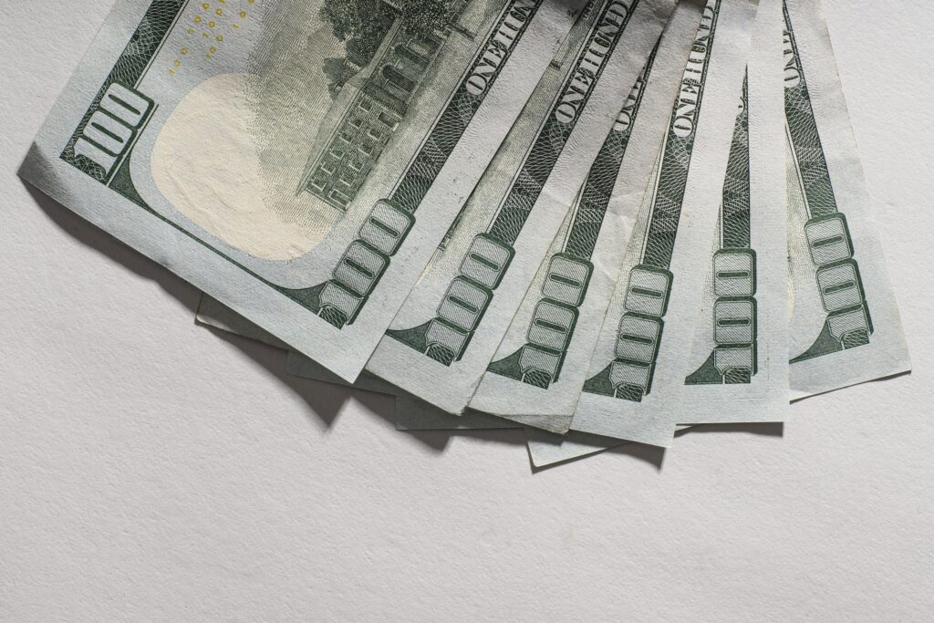 Several US $100 bills fanned out on a light surface.
