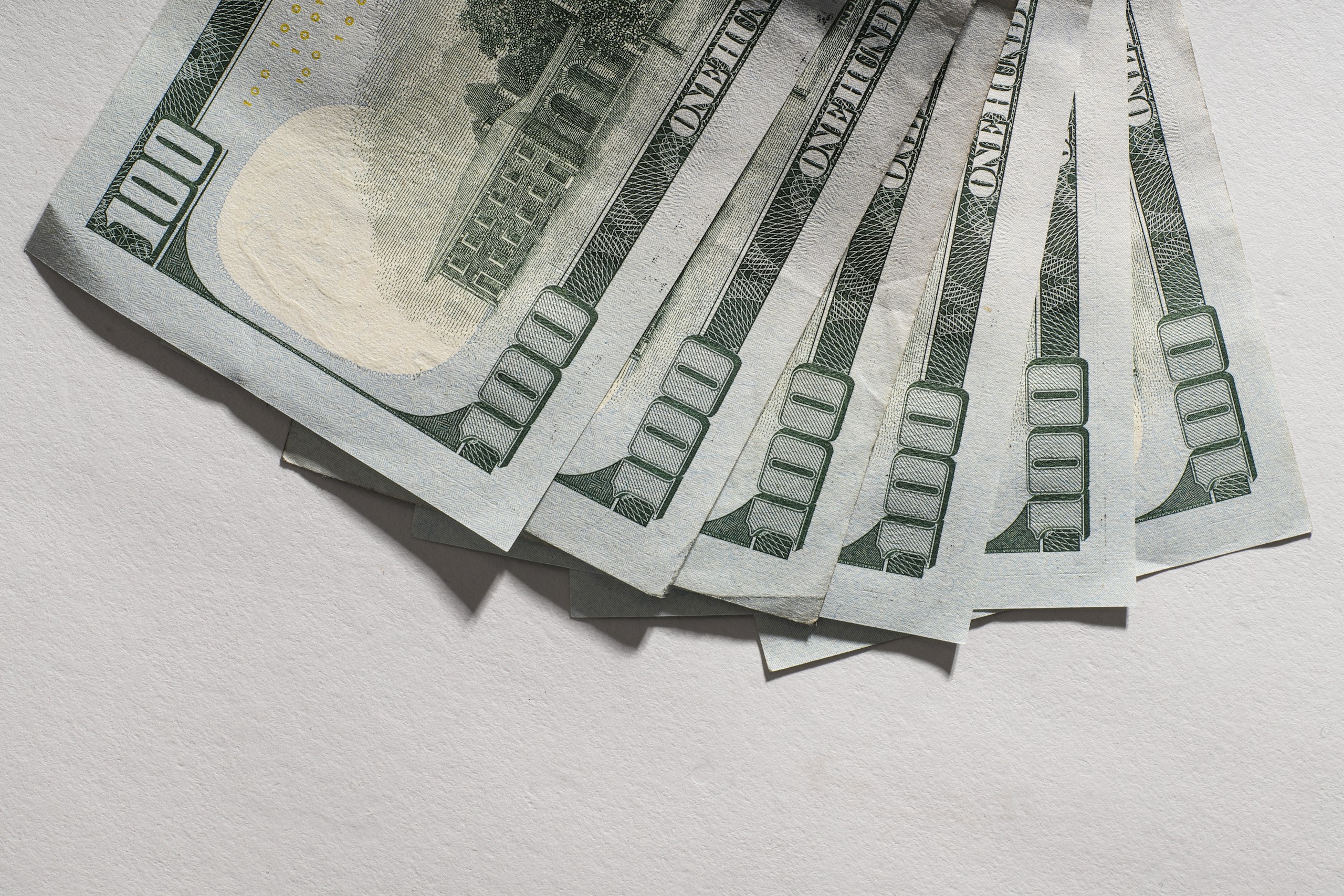 Several US $100 bills fanned out on a light surface.