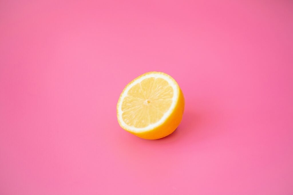 Half a lemon resting on a bright pink background, showing the juicy interior and yellow rind.