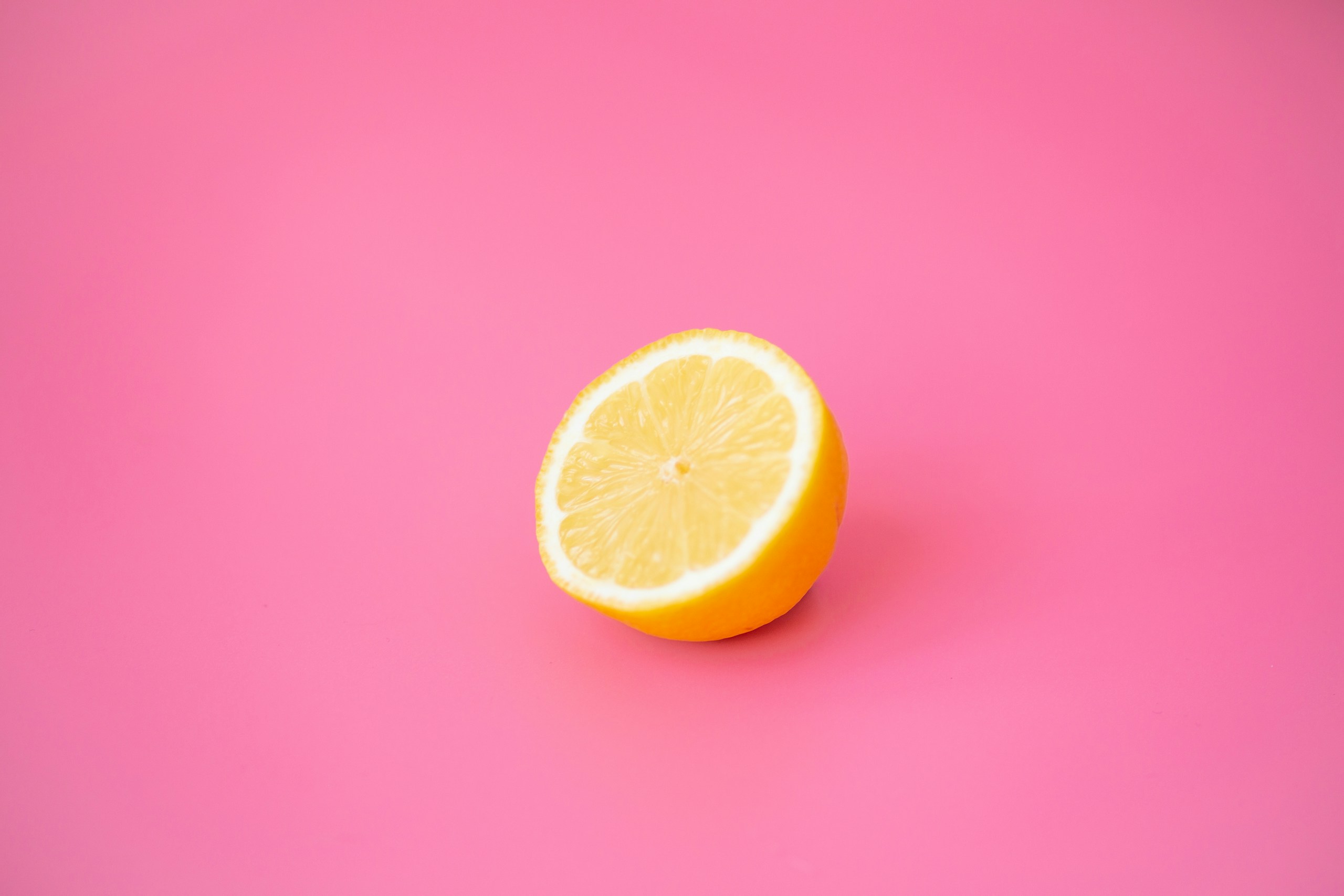 Half a lemon resting on a bright pink background, showing the juicy interior and yellow rind.
