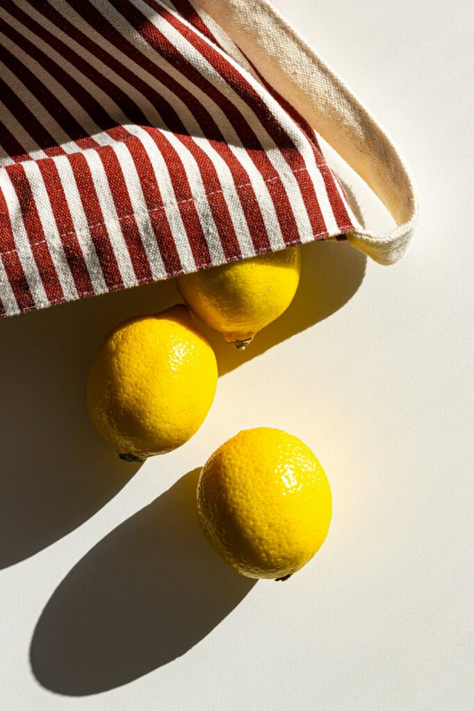 Sunlit still life of bright yellow lemons partly covered by a red-and-white striped towel against a pale background,