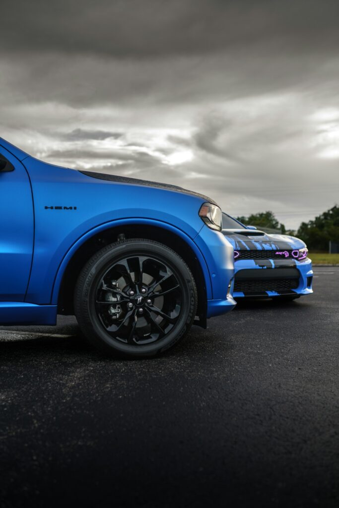 Blue pickup truck front fender and wheel in foreground with a cloudy sky overhead, dramatic lighting.