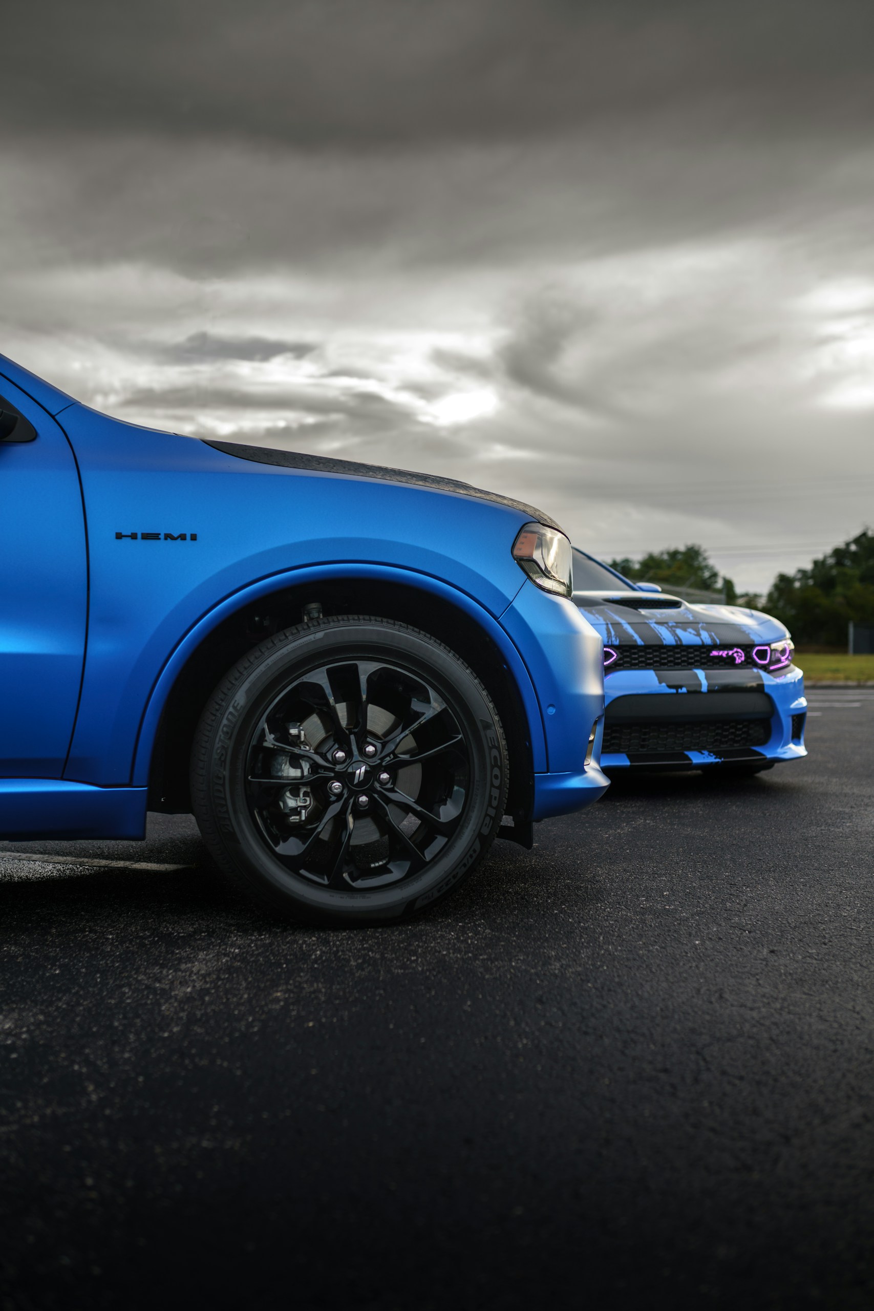 Blue pickup truck front fender and wheel in foreground with a cloudy sky overhead, dramatic lighting.