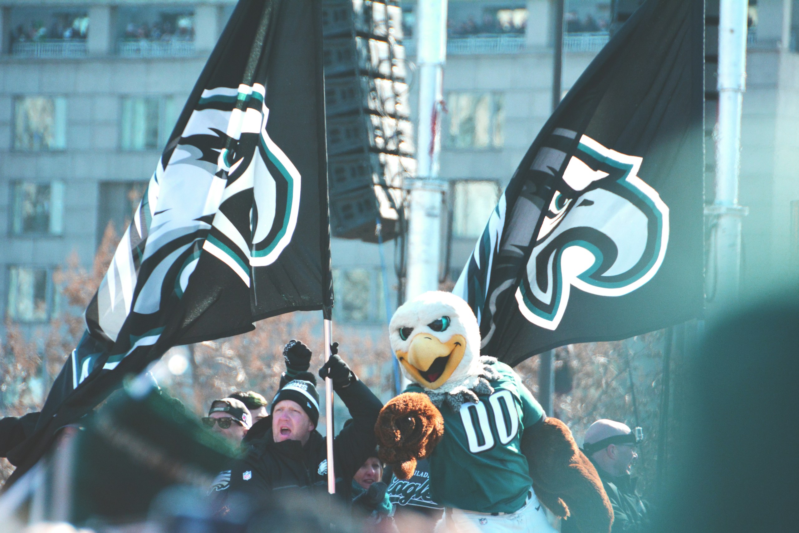 Cheering sports fans waving black and teal flags; a white eagle mascot in teal in the foreground.