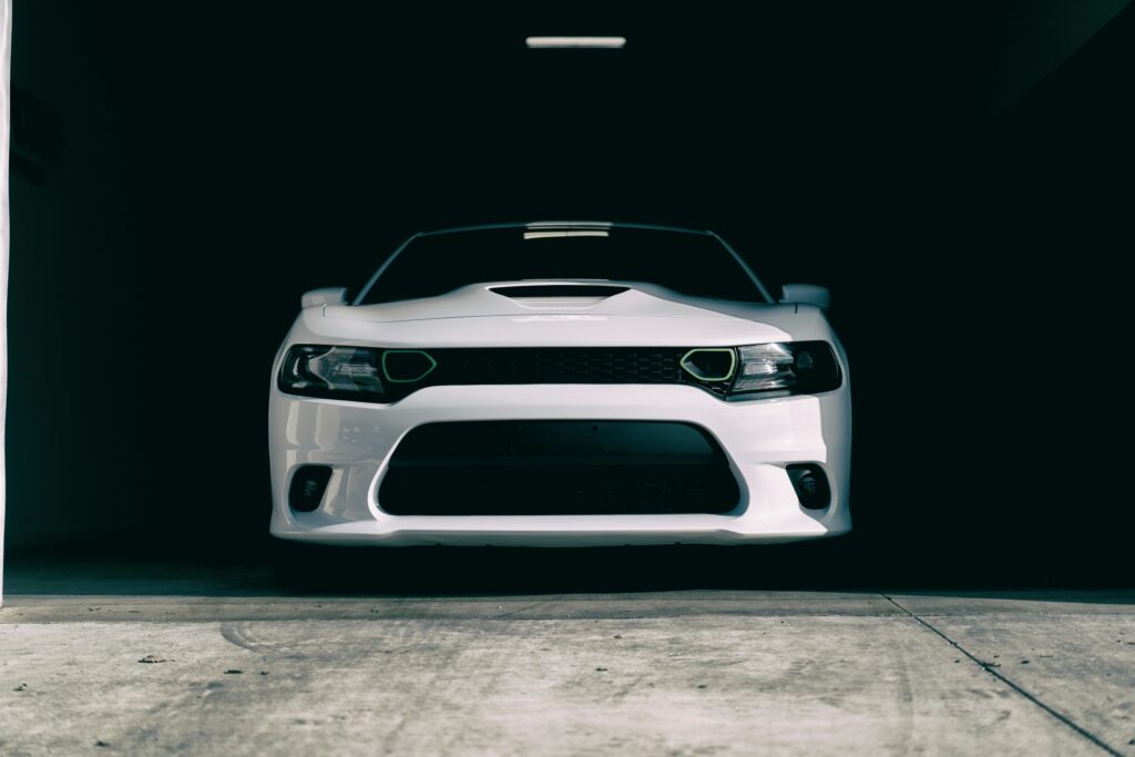 Front view of a white sports car in a dimly lit garage, with headlights and grille visible.